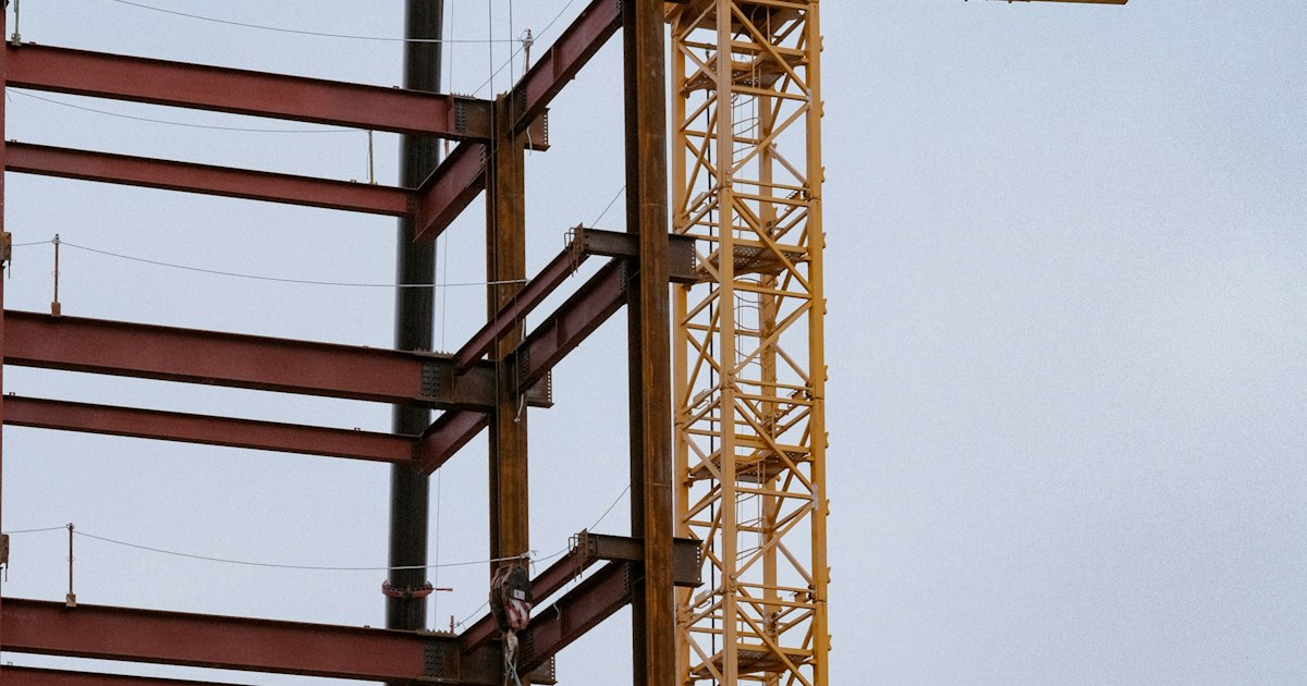 Монтаж металлического каркаса здания на стройплощадке, рядом башенный кран.
